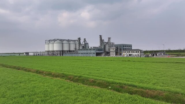 white grain silo industrial facilities beside a green field under cloudy sky