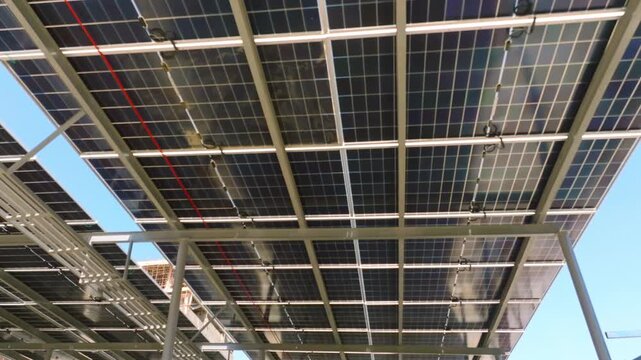 Underside view of a solar panel array canopy with metal framing, wiring and mounting hardware for renewable energy.
