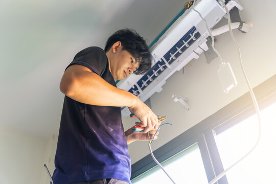 Technician installing air conditioner unit indoors, Worker wiring indoor AC unit during professional HVAC maintenance, Installation of a split-system air conditioner by technician in residential room