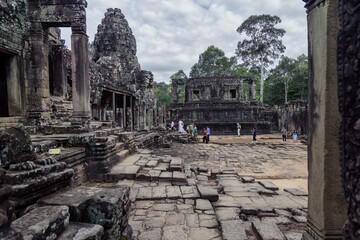 Fototapeta premium SIEM REAP, CAMBODIA, 25 October 2025 – Tourists explore the ancient Bayon temple complex in Angkor, Cambodia, marveling at its intricate stone carvings and iconic face towers under a cloudy sky.