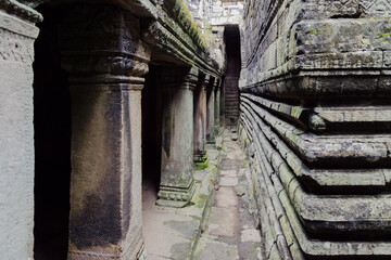 Fototapeta premium Ancient stone corridor with carved pillars and walls, moss-covered, at Bayon Temple, Angkor Wat, Siem Reap, Cambodia. The intricate architecture evokes a sense of history and mystery.