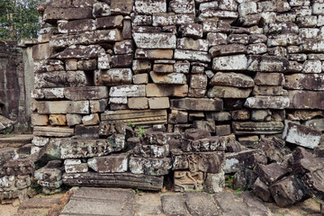Fototapeta premium Ancient stone carvings of figures and mythical creatures adorn the weathered walls of Bayon Temple, Angkor Wat, Siem Reap, Cambodia, showcasing intricate Khmer artistry.