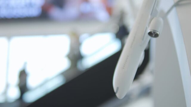 White airplane nose section hangs indoors near bright windows. Background softly blurred, showing airport-like structure. No people visible, focus on sleek aircraft detail. Ideal for travel, aviation