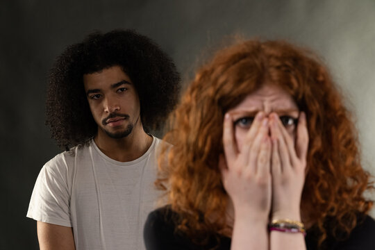 Woman covering her face in fear while man stands behind her looking hostile