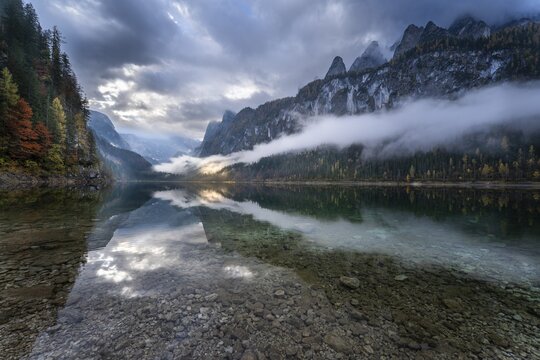 The Vordere Gosausee in autumn with a view of the Gosaukamm on the right. The Dachstein in clouds in the background. Cloudy sky. A spot of sunlight. Reflection. Vorderer Gosausee, Gosau, Gosau valley, Salzkammergut, Upper Austria, Austria