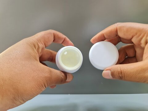 Sidoarjo, Indonesia - 24 May, 2026: Close up of hands holding a blank white plastic container of facial moisturizer day cream