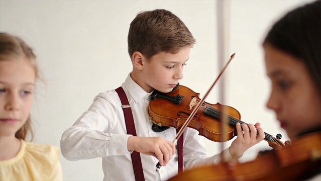 Young boy playing violin in music class, focused child learning classical instrument, school orchestra practice session with other students, education and musical talent
