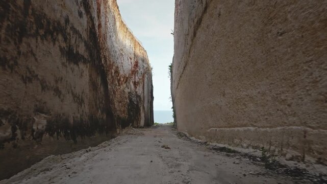 Narrow unsealed road winding through towering limestone cliffs, created by excavation, providing access to the coastline and ocean on tropical Bali island, Indonesia