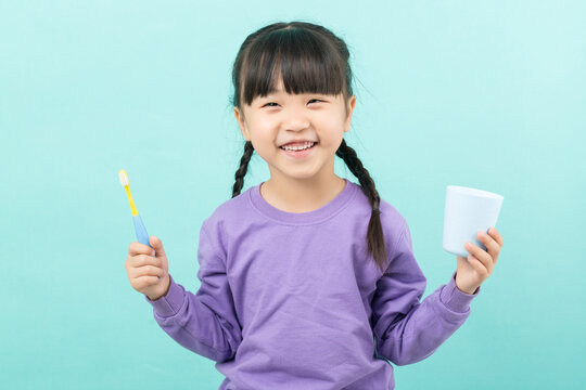 Healthy little girl brushing her teeth with a toothbrush and cup, dental hygiene and morning routine concept.
