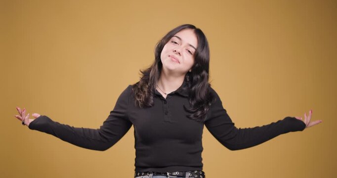 Young woman expressing uncertainty with hands outstretched on a yellow background