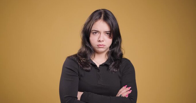 Young woman with crossed arms looking serious on a solid ochre background