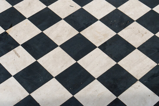 Black and white checkered floor tiles. Classic geometric pattern on polished stone. Clean lines define each square tile. Ideal for interior design projects. Subtle wear adds character to surface