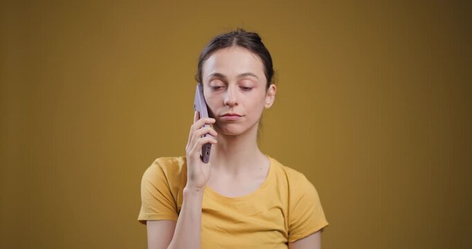 Young woman in yellow t-shirt using smartphone on ochre background