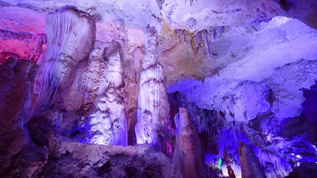 Stalactite formations illuminated by colorful lights inside a deep underground limestone cavern system