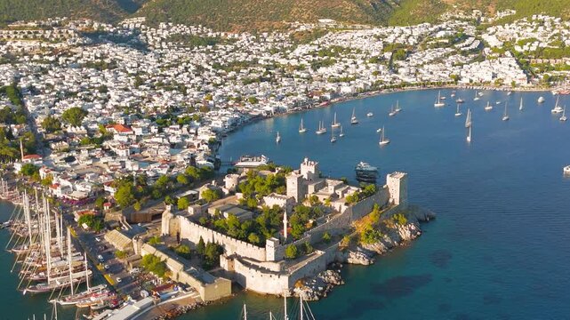 Bodrum, Turkey. Bodrum Castle, massive stone fortress walls and towers rising from a rocky peninsula, aerial drone view over the Aegean harbor with yachts at anchor. Aerial View, MasterShots, Spiral 