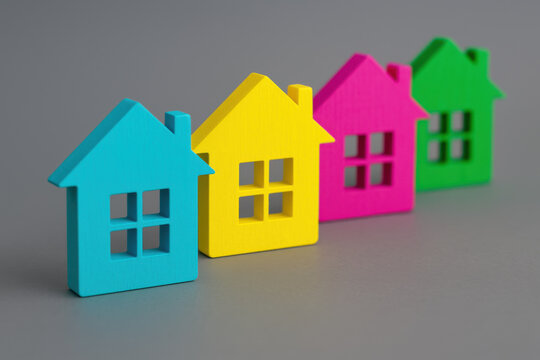 Row of colorful wooden house model in cyan yellow magenta and green color aligned diagonally on gray background representing real estate property development neighborhood