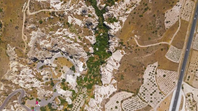Goreme, Nevsehir, Turkey. Goreme Valley, top-down aerial view over an intricate canyon system of eroded volcanic tuff, rocky cliffs, and dense green vegetation threading through the arid landscape. A