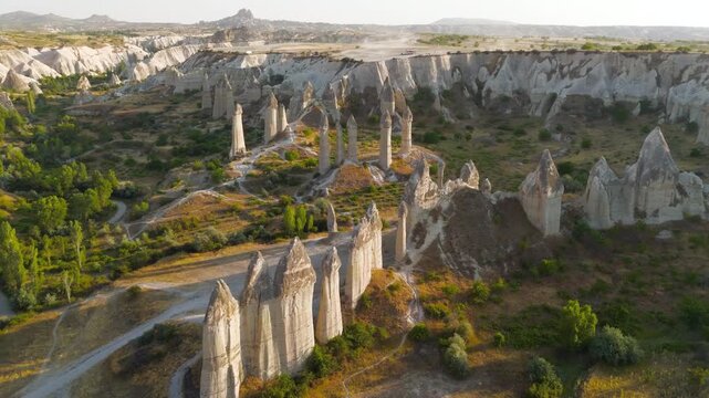 Goreme, Nevsehir, Turkey. Love Valley fairy chimneys, tall volcanic tuff pillars with dark basalt capstones, aerial view at golden hour over the eroded Cappadocian landscape. Aerial View