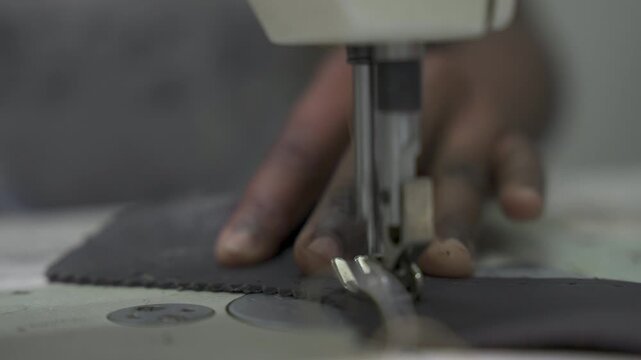A sewing machine needle moves through leather as hands guide the material. Captures the intricate process of garment making. Useful for fashion industry content.
