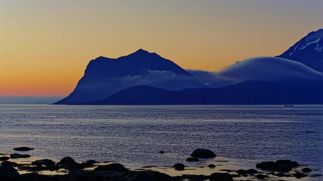 Arctic summer Time Lapse: fishing boat out for fishing while cold midnight sea fog takes over the fjord and the mountains. Lofoten Islands, Northern Norway.