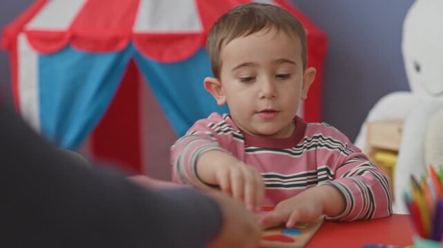 Boy placing colorful wooden puzzle shapes with hands at a red table in a studio, sorting pieces and pointing with finger; early learning concentration.