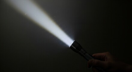 Fototapeta premium A hand holding a bright LED flashlight shining a beam of light in the dark.