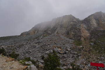 Naklejka premium Dramatic Mountain Landscape Under Cloudy Skies with Rocky Terrain and Fog.