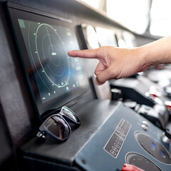 Captain hand pointing at marine radar monitor screen or GPS navigation map on boat dashboard. Nautical vessel control system in wheelhouse or ship bridge. Modern boating technology and operation © zephyr_p