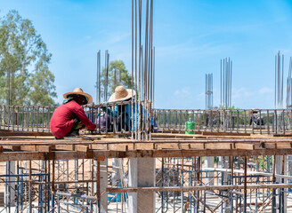 Construction workers manually tying steel rebar reinforcement cages for concrete beams on a building site framework under a clear blue sky. © Zblaster