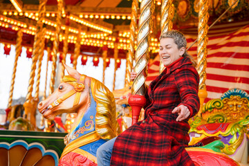 Fototapeta premium Woman enjoys riding horse on carousel at amusement park during winter morning with bright lights