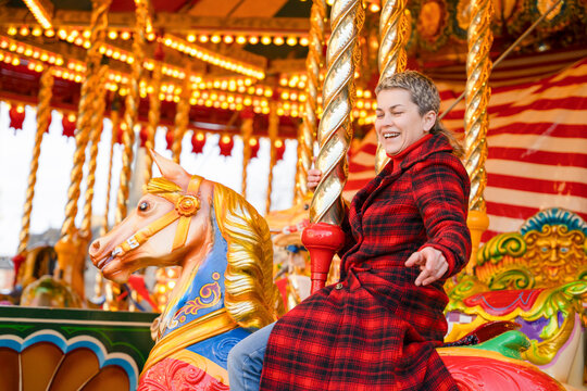 Woman enjoys riding horse on carousel at amusement park during winter morning with bright lights