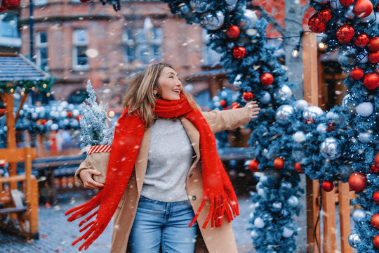 Woman enjoys winter market while holding a gift near festive decorations in a snowy setting during the holiday season