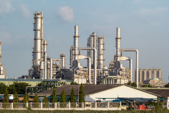 Industrial landscape in Map Ta Phut Industrial Estate, Rayong Province, Thailand, refinery complex with towering distillation columns, intricate pipelines, and massive storage tanks beneath blue sky.