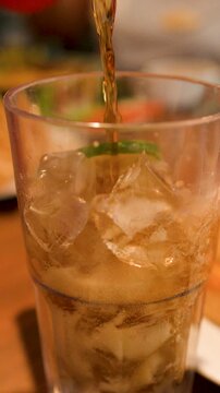 Pouring Dark Cola Into a Glass with Ice and Lemon Slice
