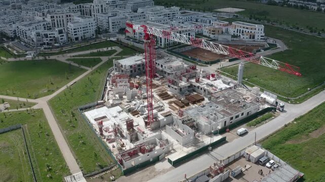 360-degree aerial orbit around a tower crane above a residential construction site, revealing a large urban development with buildings, roads and green spaces.
