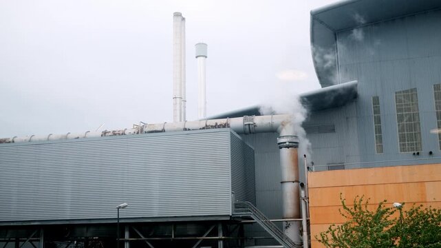 Exterior view of a waste treatment and energy recovery facility with industrial stacks, metal structures and steam rising from the site in France.