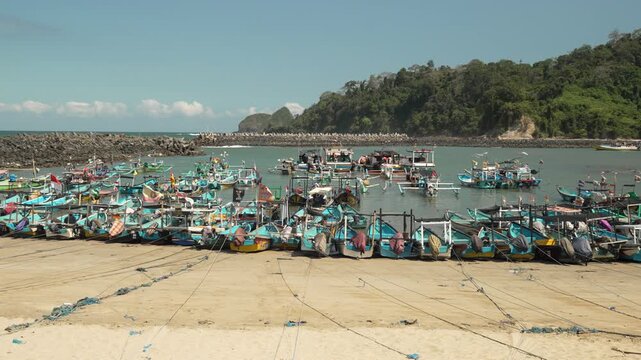 Docked fishing boats lined up along sandy shore in small coastal harbor in sunlight