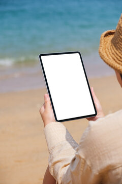 Vertical mockup image of a woman holding a digital tablet with blank desktop screen by the sea