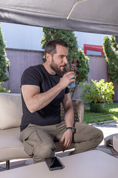 Handsome young bearded man drinking a blue cocktail at a lounge bar terrace