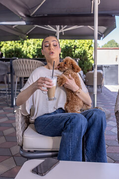 Young woman holding an iced coffee and cuddling a small puppy at a cafe