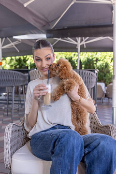 Portrait of a smiling young woman holding her cute puppy at an outdoor cafe