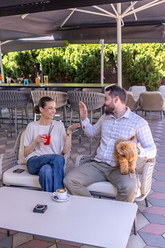 Happy couple high fiving and laughing at a cafe terrace with a puppy