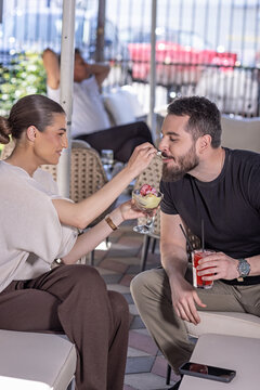 Young woman playfully feeding ice cream to her boyfriend at an outdoor restaurant