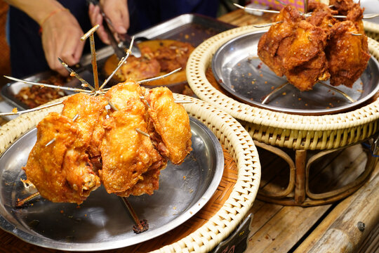 Close up of golden brown crispy deep fried chicken portions displayed on a traditional rattan pedestal tray (Khantoke) at a local food market stall.