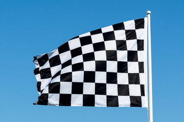 Obraz premium Black and white checkered flag flutters against a clear blue sky. Wind carries the flag with dynamic motion.