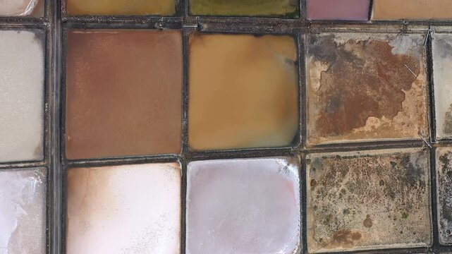 Shapes of salt flats mix different colors like pink, brown, and white. The sun shines on these flat areas, highlighting their unique patterns and textures.
