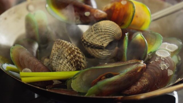 Home cook boiling fresh green mussels and blood cockle for a seafood meal