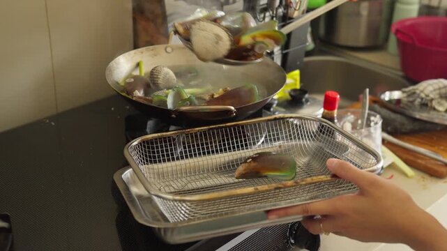 A person draining freshly boiled seafood in a colander before stir-frying it with a sweet and spicy sauce