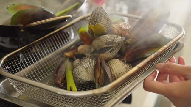 A person draining freshly boiled seafood in a colander before stir-frying it with a sweet and spicy sauce
