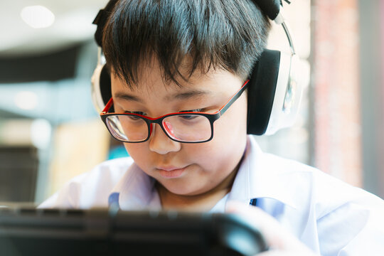 Asian boy wearing glasses and headphones using a digital tablet for online learning or gaming. Concept of modern education, childhood technology, e-learning and entertainment.